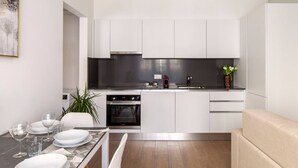 Une cuisine moderne avec des meubles blancs, un plan de travail noir et un coin repas avec une table dressée pour quatre personnes.