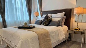 Una cama bien hecha con una bandeja de aperitivos y vasos, una lámpara de noche y una mesita de noche.