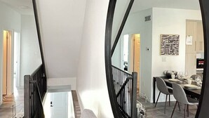 Una sala moderna con un espejo grande, una escalera y un comedor.