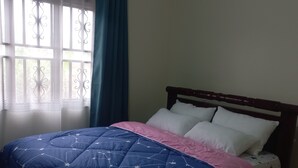 Un dormitorio con cama, ventana con cortinas y una lámpara de pared.