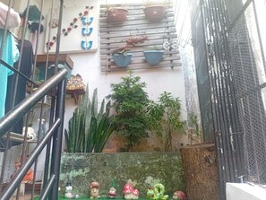 Un petit espace extérieur avec un escalier en métal, des plantes en pot et des objets décoratifs, notamment un bonhomme de neige et des figurines de champignons.