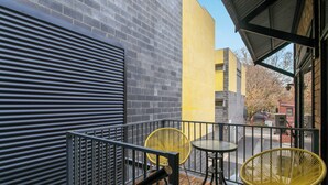 A balcony with a metal railing, two yellow chairs, and a table. - Cozy Stays - Private Rooms (Adelaide)