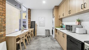 A modern kitchen with wooden cabinets, a built-in microwave, and a dishwasher. - Cozy Stays - Private Rooms (Adelaide)