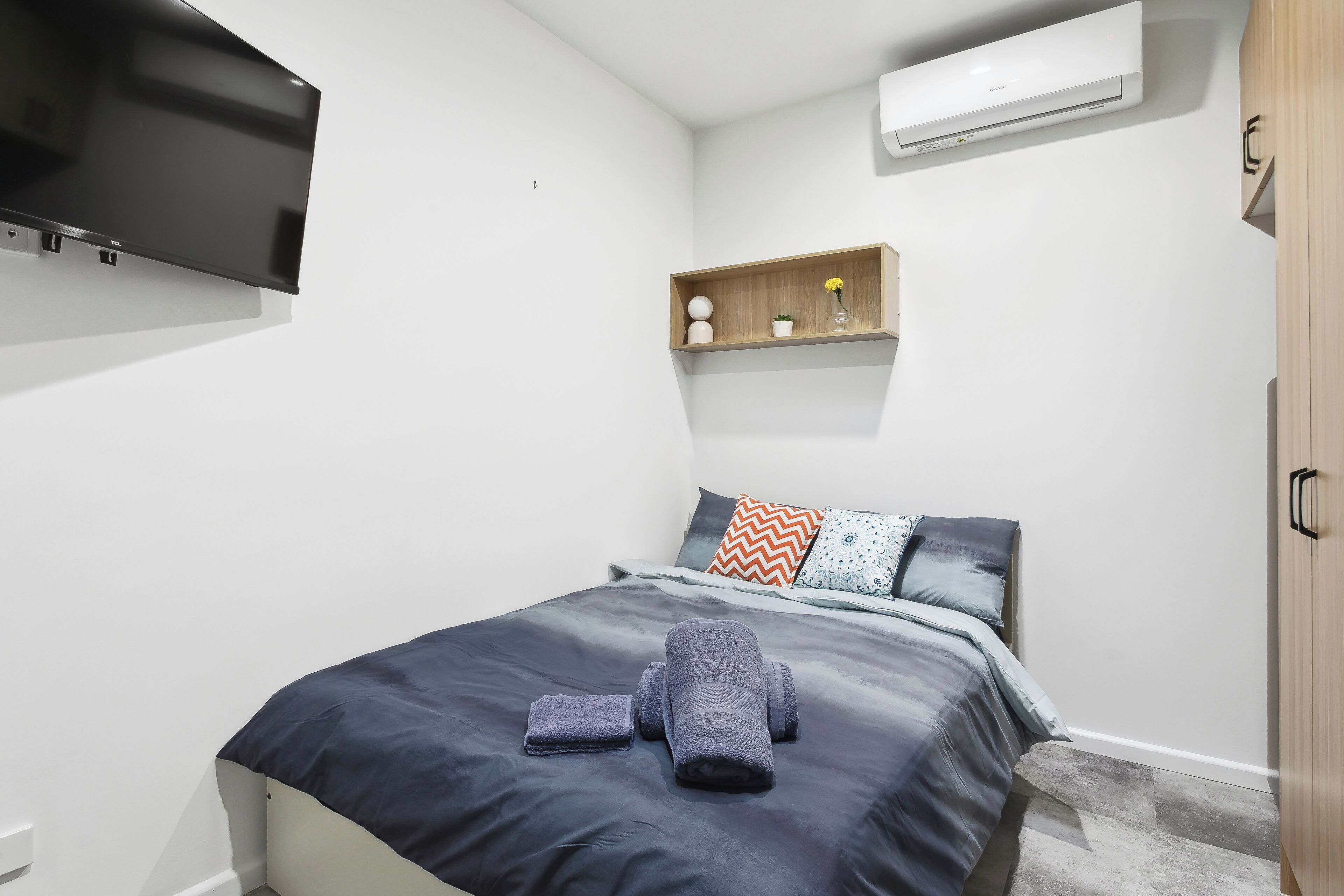A modern bedroom with a bed, a flat-screen TV, a shelf with decorative items, and a wardrobe.