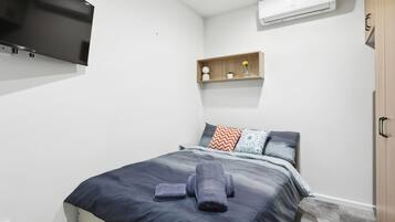 A modern bedroom with a bed, a flat-screen TV, a shelf with decorative items, and a wardrobe.