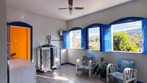 A spacious room with a tiled floor, a ceiling fan, a window with blue shutters, and a seating area with two chairs and a small table. - Pousada Lavramor (Lençóis)