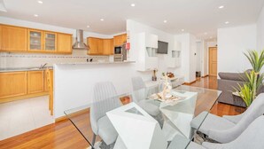 Une cuisine moderne avec des meubles en bois, une table à manger en verre et un canapé gris dans un salon lumineux.