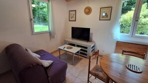 A cozy room with a purple sofa, a small table, a TV on a white stand, and a dining table with chairs.