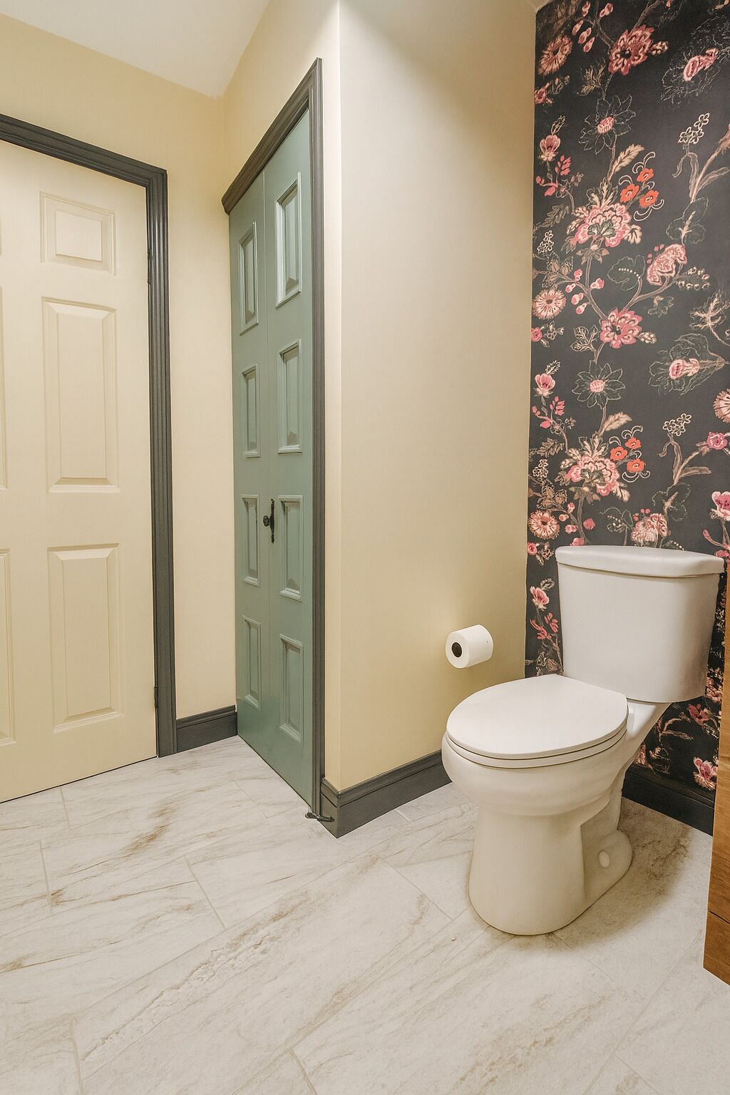 Casa de banho com sanita, porta verde e papel de parede floral.