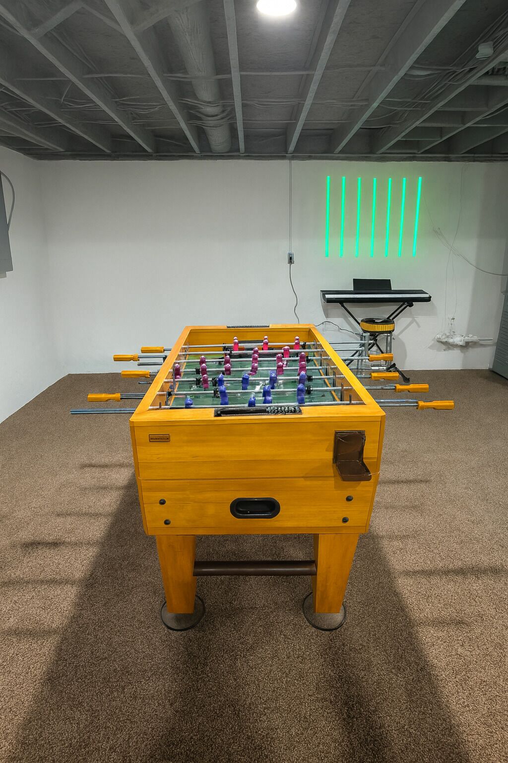 A foosball table in a room with a carpeted floor and a ceiling with exposed beams.