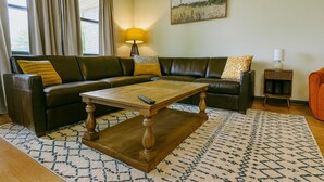 Ein Wohnzimmer mit einem dunkelbraunen Ledersofa, einem Holztisch und gemusterten Teppichen.