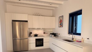 A modern kitchen with white cabinetry, a stainless steel refrigerator, a built-in oven, and a window with a view. - 4-Bedroom Villa in Milos, Seaview and Sunset view, Private Pools (Milos)