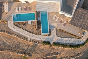 An aerial view of a resort with multiple swimming pools, a covered area, and a stone pathway.