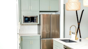 Une cuisine moderne avec des meubles de couleur vert clair, des appareils en acier inoxydable et un plan de travail blanc.