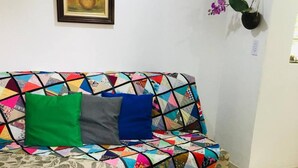 A sofa with a colorful quilt, a patterned rug, and a framed painting on the wall. - Compact Tiny House Bambuzal (Paty do Alferes)