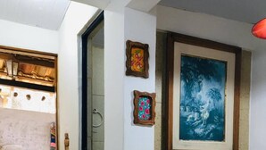 A room with a tiled floor, a wooden door, a framed painting, a potted plant, and a colorful quilt on the floor. - Compact Tiny House Bambuzal (Paty do Alferes)