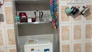 A compact kitchen with a white refrigerator, a microwave, and a sink. There are various kitchen utensils and a coffee maker on the shelves. - Compact Tiny House Bambuzal (Paty do Alferes)