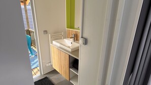 A modern bathroom with a white sink, wooden cabinet, and a green mirror. - Mobilhome cap ferret (Lège-Cap-Ferret)