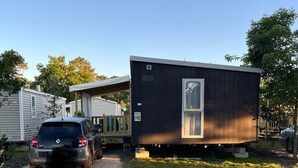 A modern mobile home with a gravel driveway, a parked car, and a small deck area. - Mobilhome cap ferret (Lège-Cap-Ferret)