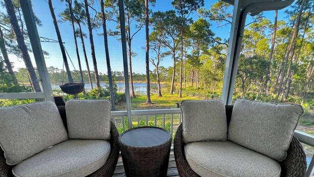 A porch with wicker chairs and a small table, overlooking a lake and trees. - Point & Paddle
Waterfront Retreat @Alligator Point (Alligator Point)