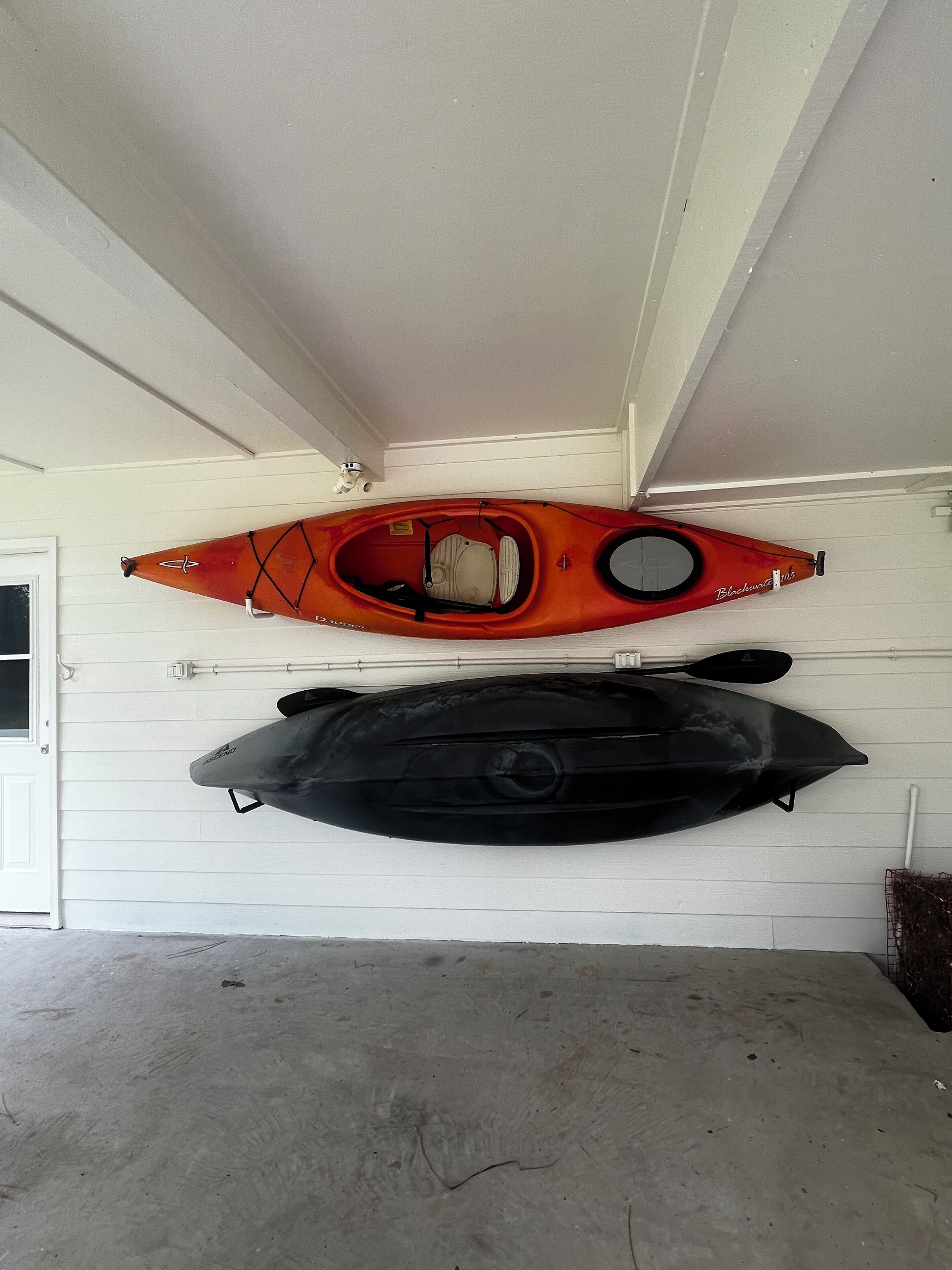 Two kayaks mounted on a garage wall, one orange and one black.