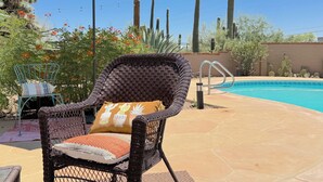 Une chaise en osier avec un coussin, une piscine et des cactus en arrière-plan.