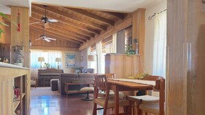 Un vaste espace de vie agrémenté de poutres en bois, une table à manger avec des chaises, un canapé et un coin cuisine équipé d’une cuisinière et de placards.