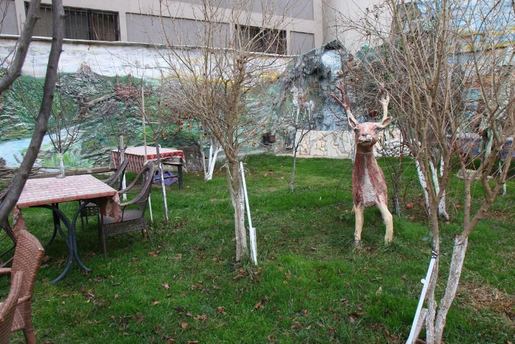 Un patio con una estatua de un ciervo, una mesa, sillas y un mural en la pared.