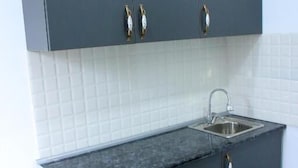 Een keuken met donkere kastjes, een witte betegelde spatwand en een roestvrijstalen spoelbak.