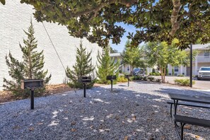 Une terrasse en gravier, agrémentée de bancs et de mangeoires à oiseaux, entourée d’arbres et d’un bâtiment à la façade blanche.