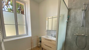 Un baño moderno con cabina de ducha de vidrio, suelo de madera, una ventana pequeña y una alfombra verde.