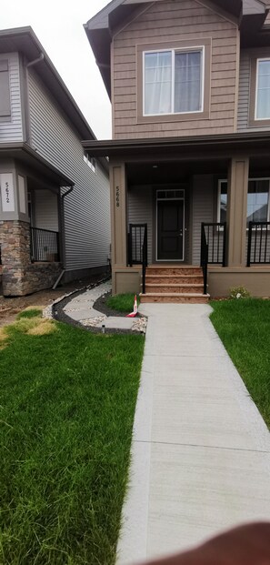 A two-story residential house with a front porch, a stone foundation, and a well-maintained lawn.