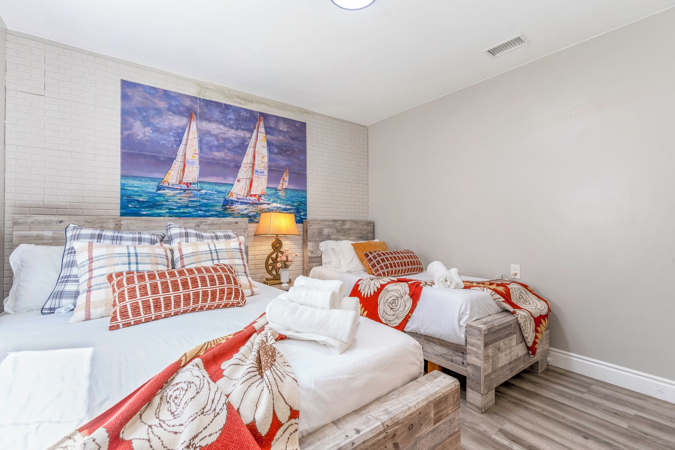 A hotel room with two beds, a painting of sailboats, a lamp, and a wooden headboard.