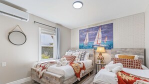 Ett hotellrum med två sängar i trä, en målning som föreställer segelbåtar, en rund spegel och ett fönster med gardiner.