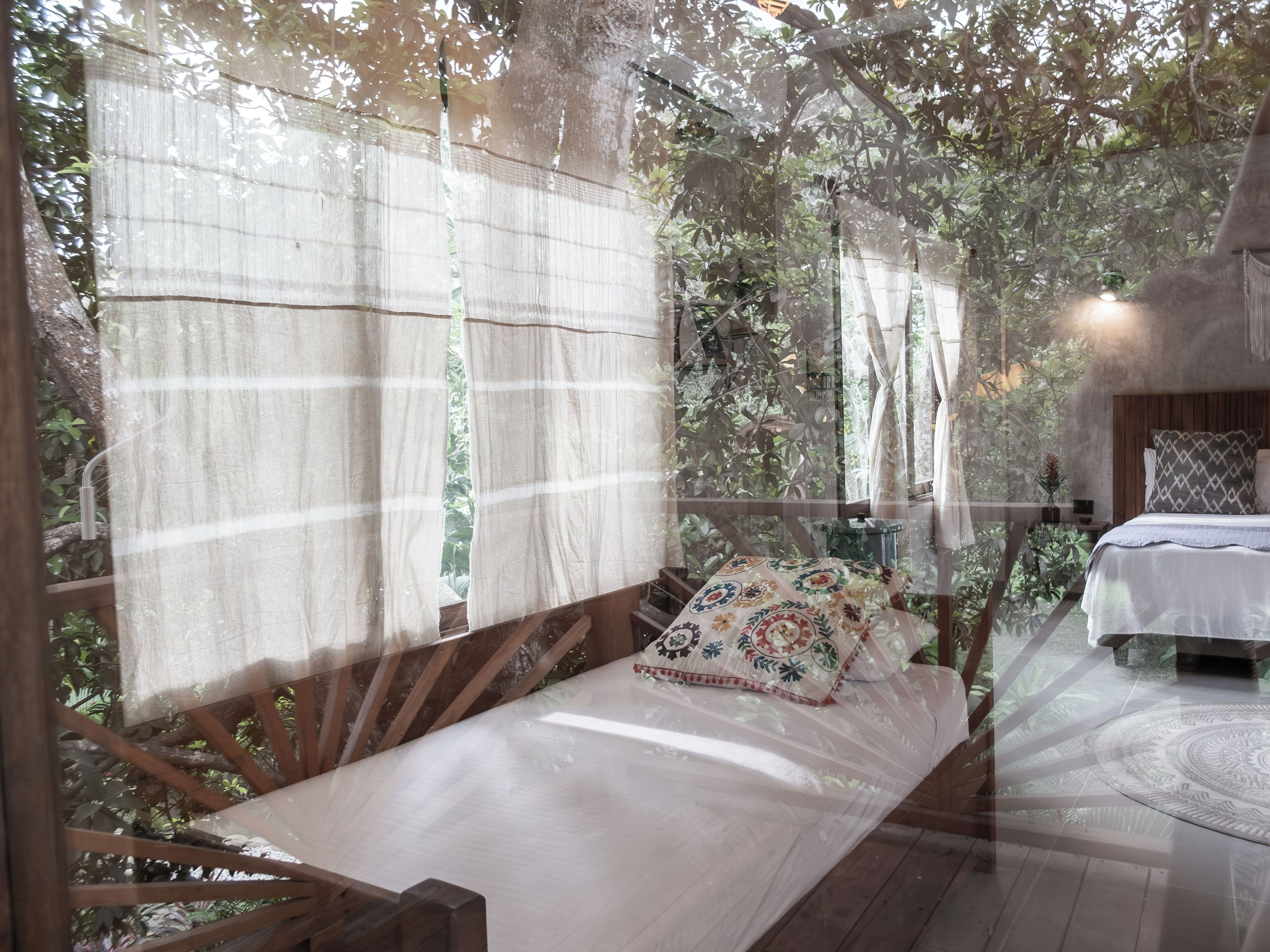 A bedroom with a wooden bed, a small bedside table, and a window with a view of greenery.