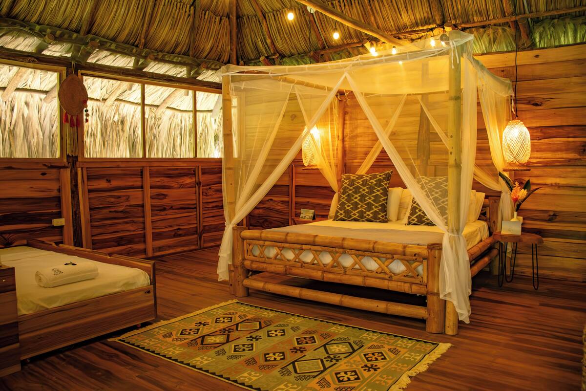 Um quarto de madeira com uma cama, uma cama menor e uma mesa de cabeceira com abajur.