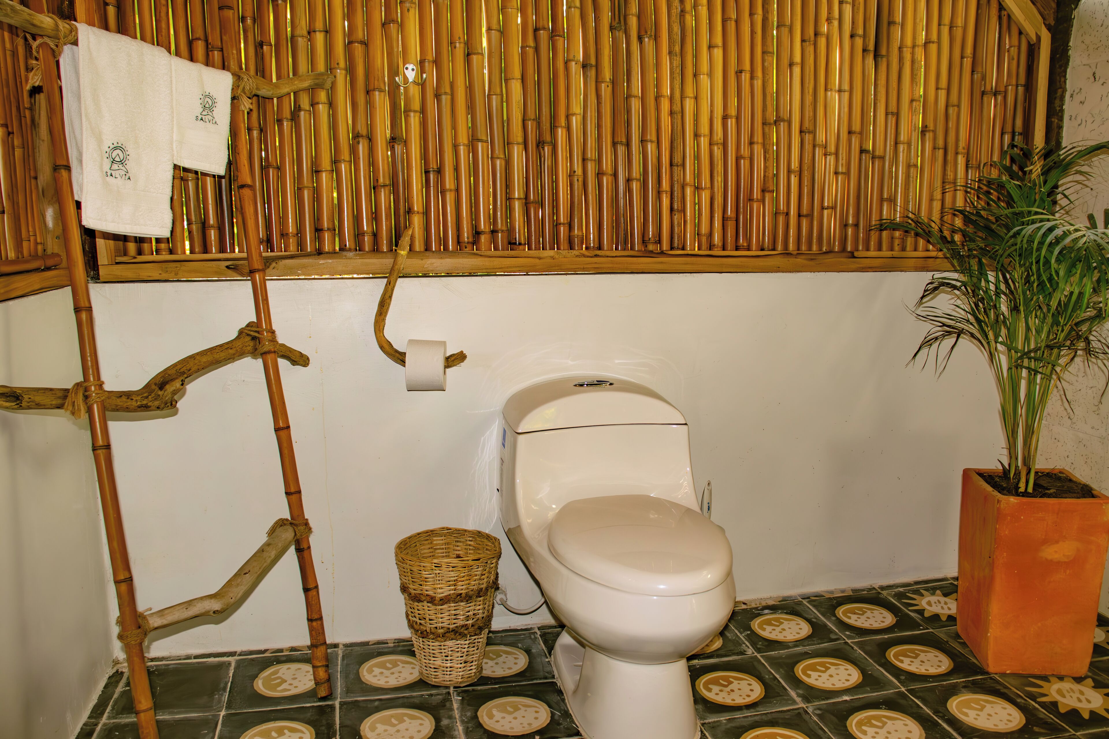 Een badkamer met toilet, bamboe wand en een potplant.