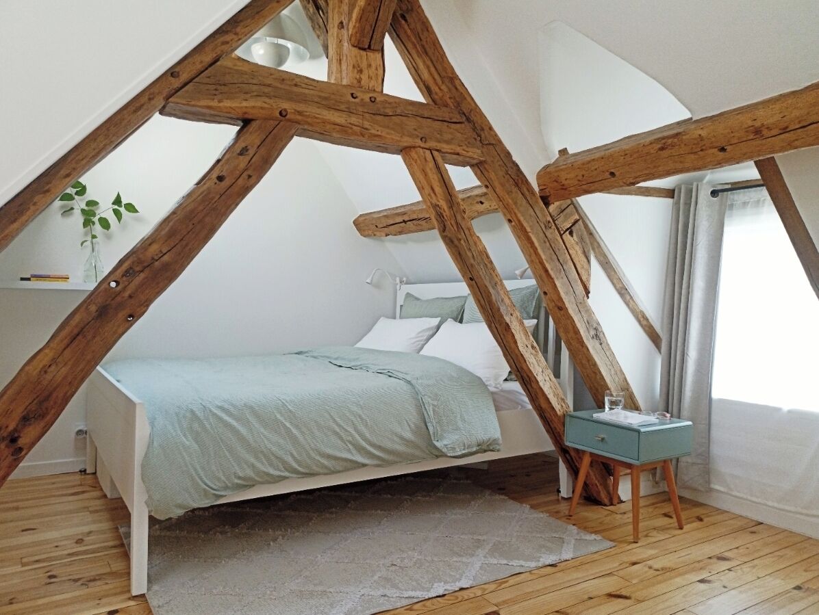 Ein Schlafzimmer mit schräg versiegelter Decke, einem Bett, einem Nachttisch und einer kleinen Pflanze.
