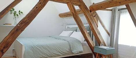 Ein Schlafzimmer mit schräg versiegelter Decke, einem Bett, einem Nachttisch und einer kleinen Pflanze.