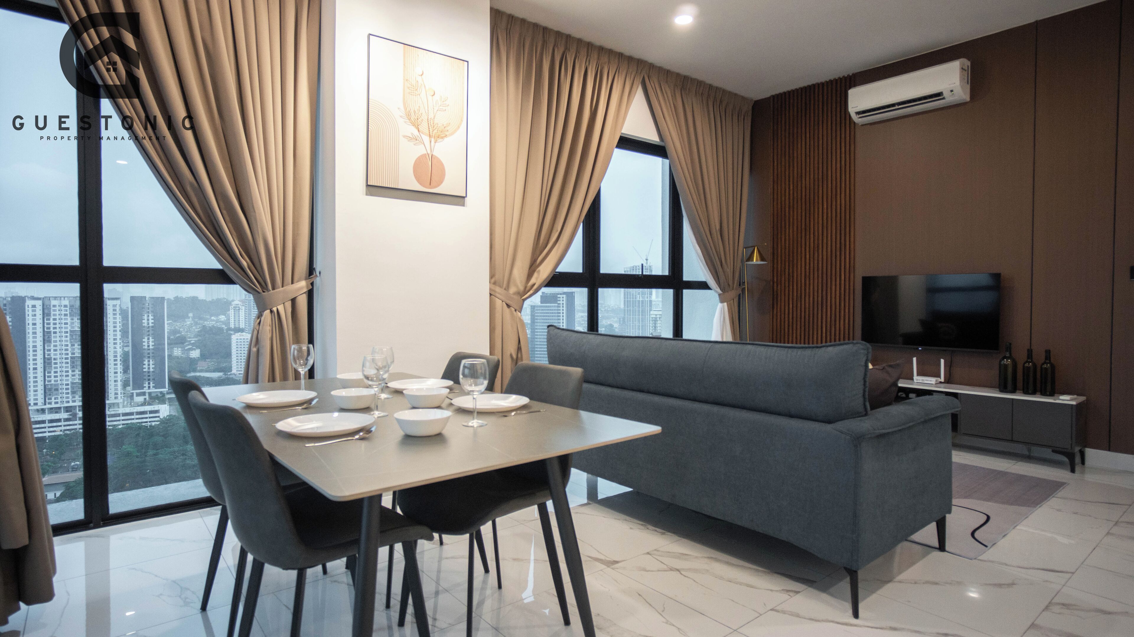 A modern living room with a dining area, grey sofa, and a flat-screen TV.