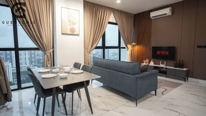 A modern living room with a dining area, a grey sofa, a flat-screen TV, and a city view.