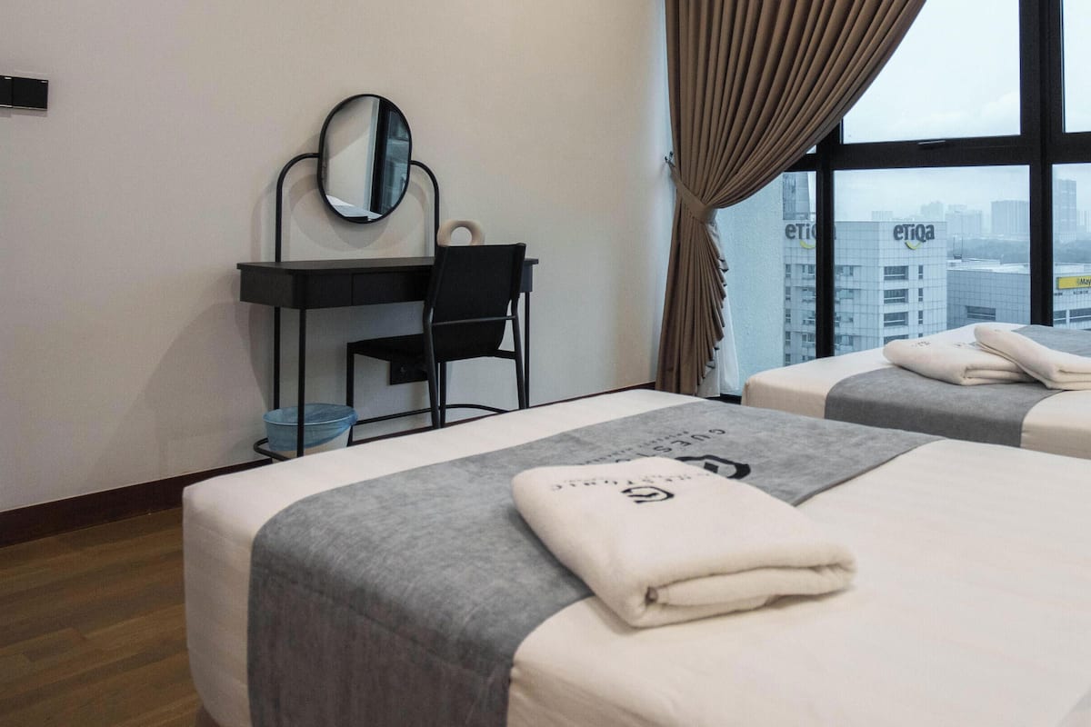 Une chambre d’hôtel avec deux lits, un bureau avec une chaise, un miroir et une vue sur le paysage urbain grâce à de grandes fenêtres.