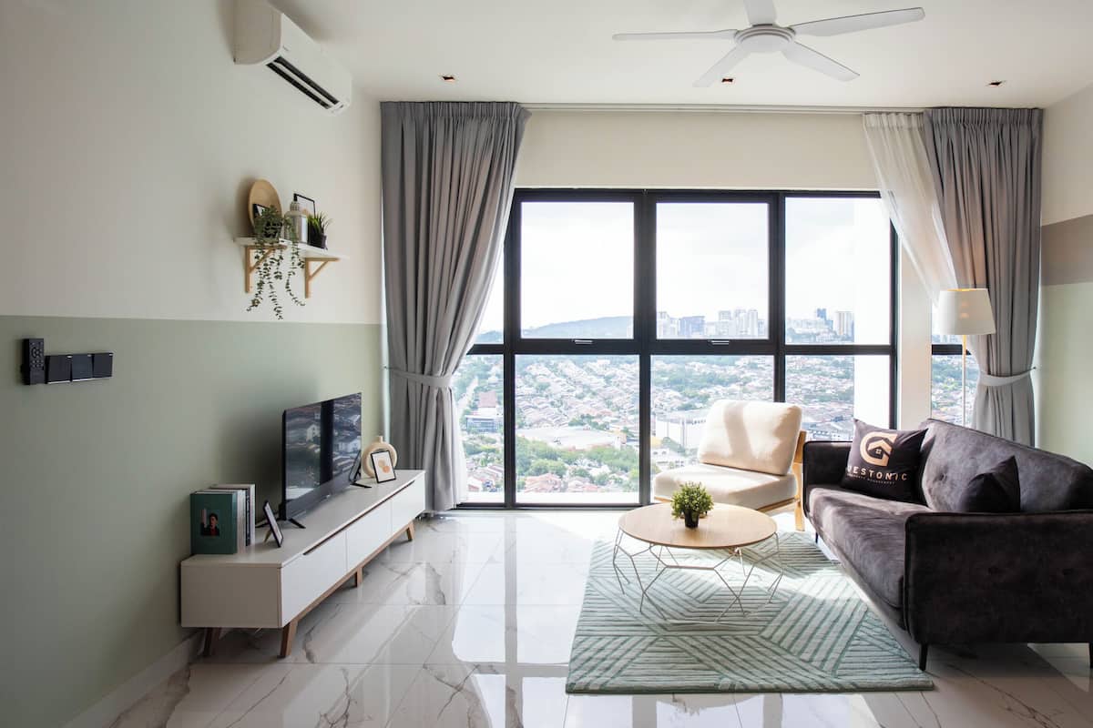 Un salon moderne avec un canapé, une table basse et un téléviseur posé sur un meuble. Il y a une grande fenêtre avec des rideaux, un ventilateur de plafond et une vue sur le paysage urbain.