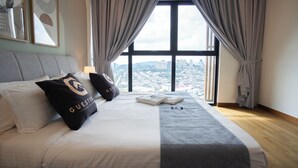 A hotel room with a large bed, grey curtains, and a view of a cityscape.