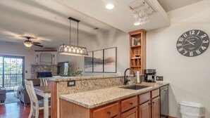A kitchen with granite countertops, wooden cabinets, a built-in dishwasher, and a large wall clock. - 2BR Village At Indian Point 1202 near SDC-Free Tickets Daily up to $500 (Branson)