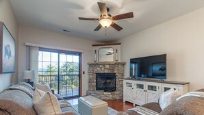 A living room with a stone fireplace, a ceiling fan, a television, and a large window. - 2BR Village At Indian Point 1202 near SDC-Free Tickets Daily up to $500 (Branson)
