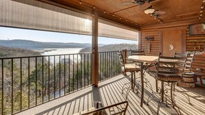Eine Holzterrasse mit Tisch und Stühlen, mit Blick auf einen See und bewaldete Hügel.