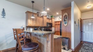 Eine Küche mit Holzschränken, einer Granit-Arbeitsplatte, einem Edelstahl-Kühlschrank und einem Mülleimer.
