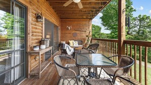 Eine Holzterrasse mit Korbmöbeln, einem Glastisch und einem Deckenventilator.