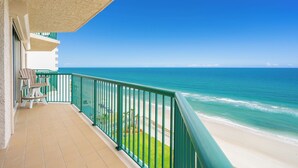 Un balcon avec vue sur l’océan, une rambarde verte et quelques chaises.